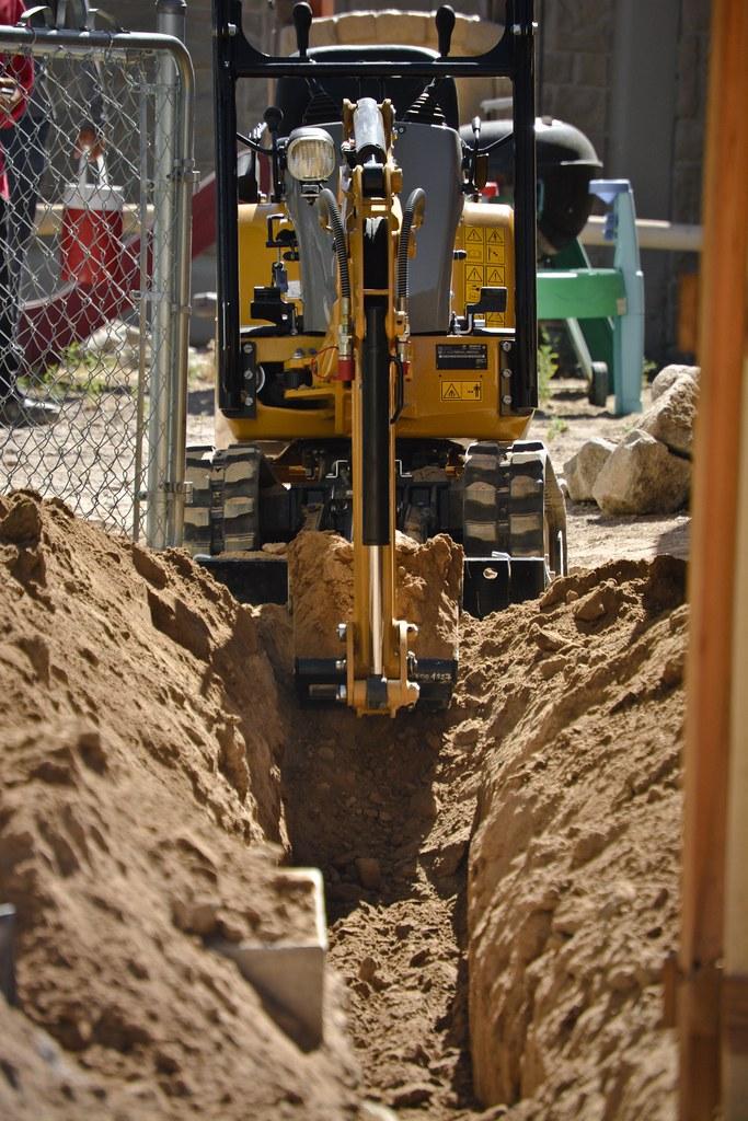 Compact excavator cutting a clean trench through a residential yard
