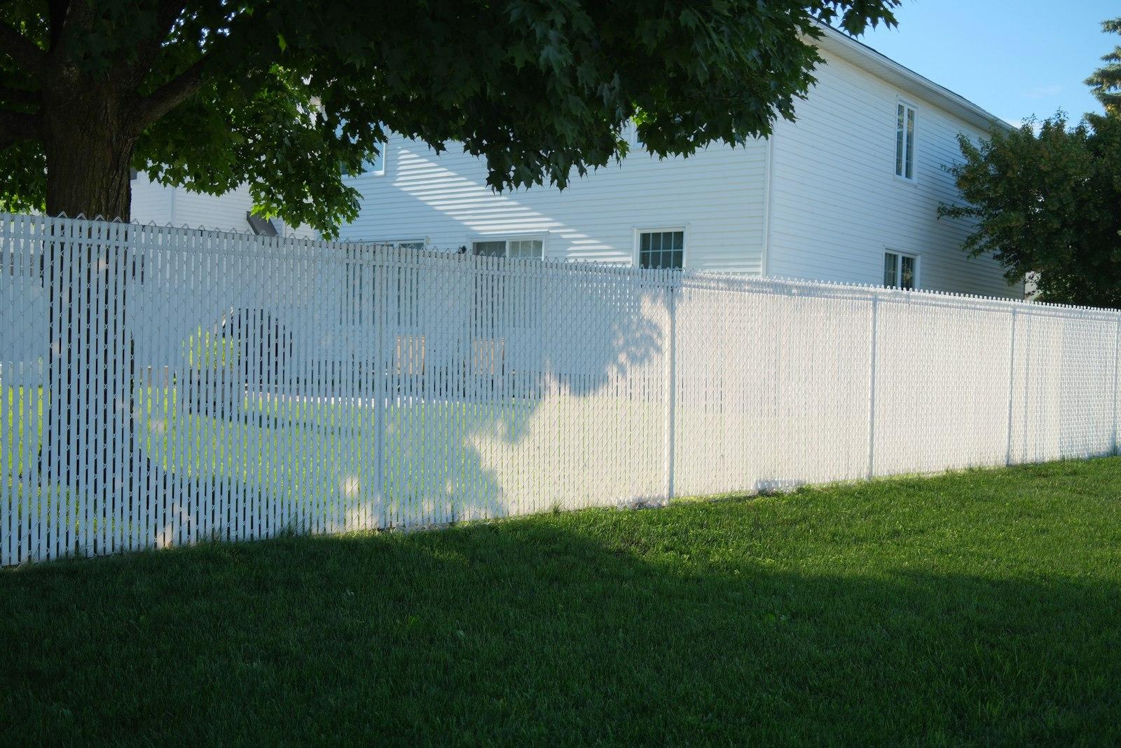 Tall white vinyl privacy fence framing a two-story suburban Michigan home with a mature maple tree and green lawn