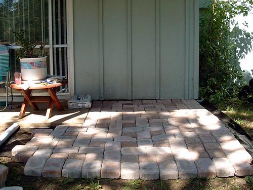 Homeowner's backyard paver patio being laid course by course against the house